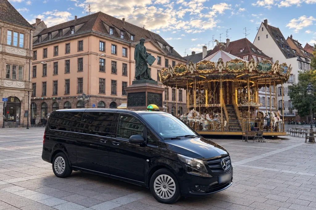 Van Mercedes taxi sur la place Gutenberg, devant la statue et le carrousel.